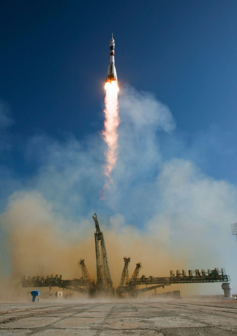 A rocket lifting off from a launch pad in a cloud of fire and smoke against a clear blue sky