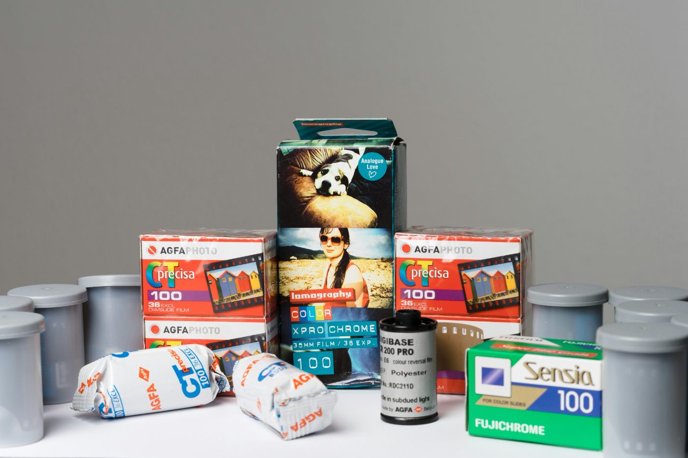Boxes and rolls of 35mm color slide film stacked on a white table among empty grey film canisters.