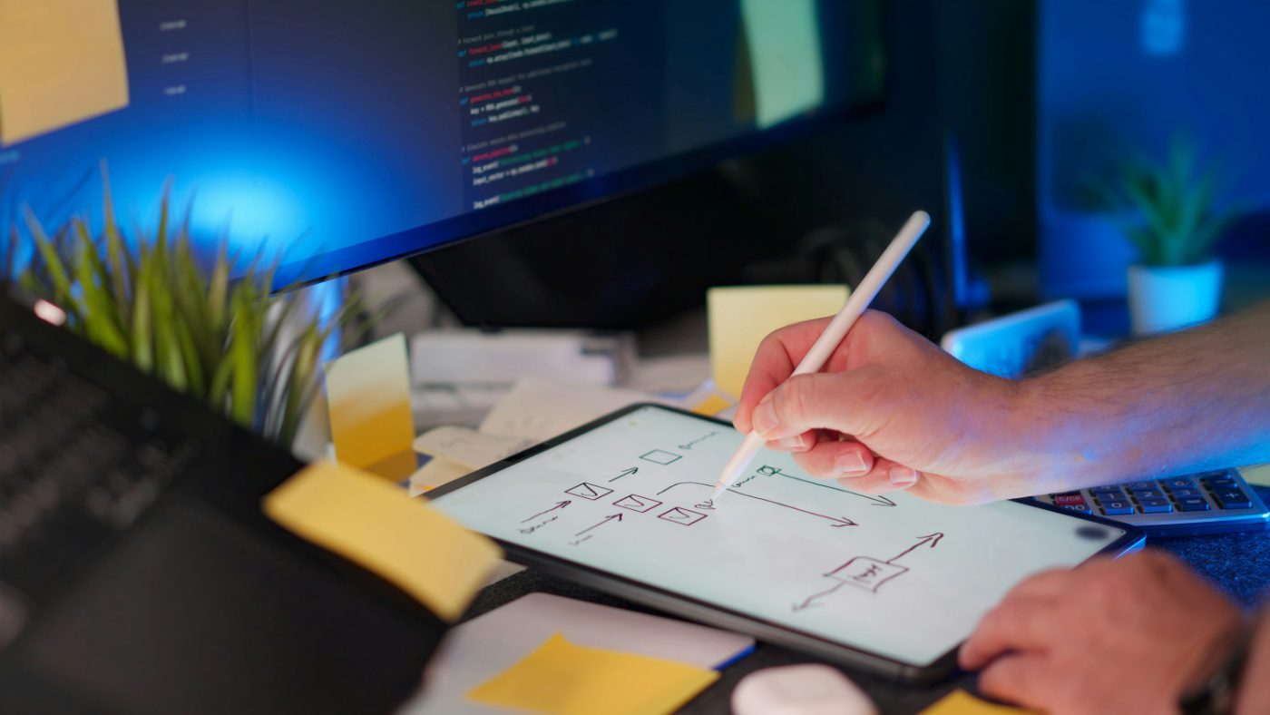 Workflow mapped out on a tablet beside code on screen